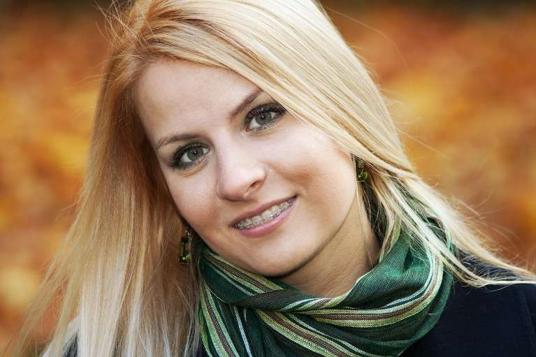 Blonde woman wearing a green scarf smiling, representing potential signs you might need braces