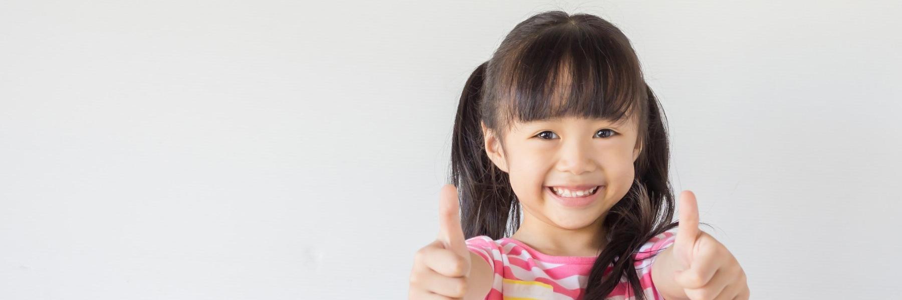 Young girl holding two thumbs up at pediatric dentist near me Northborough